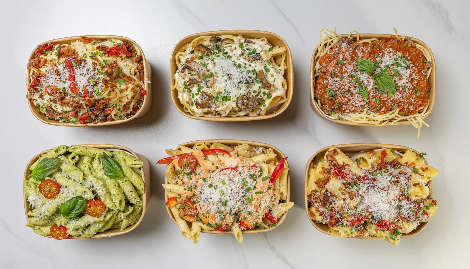 Six plateaux de pâtes Le Pastaman vus de haut sur le marbre : bolognaise, rosa, pesto, Alfredo, carbonara.